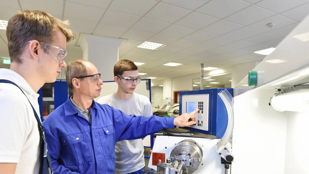 Junge Auszubildende werden an einer CNC-Maschine trainiert.