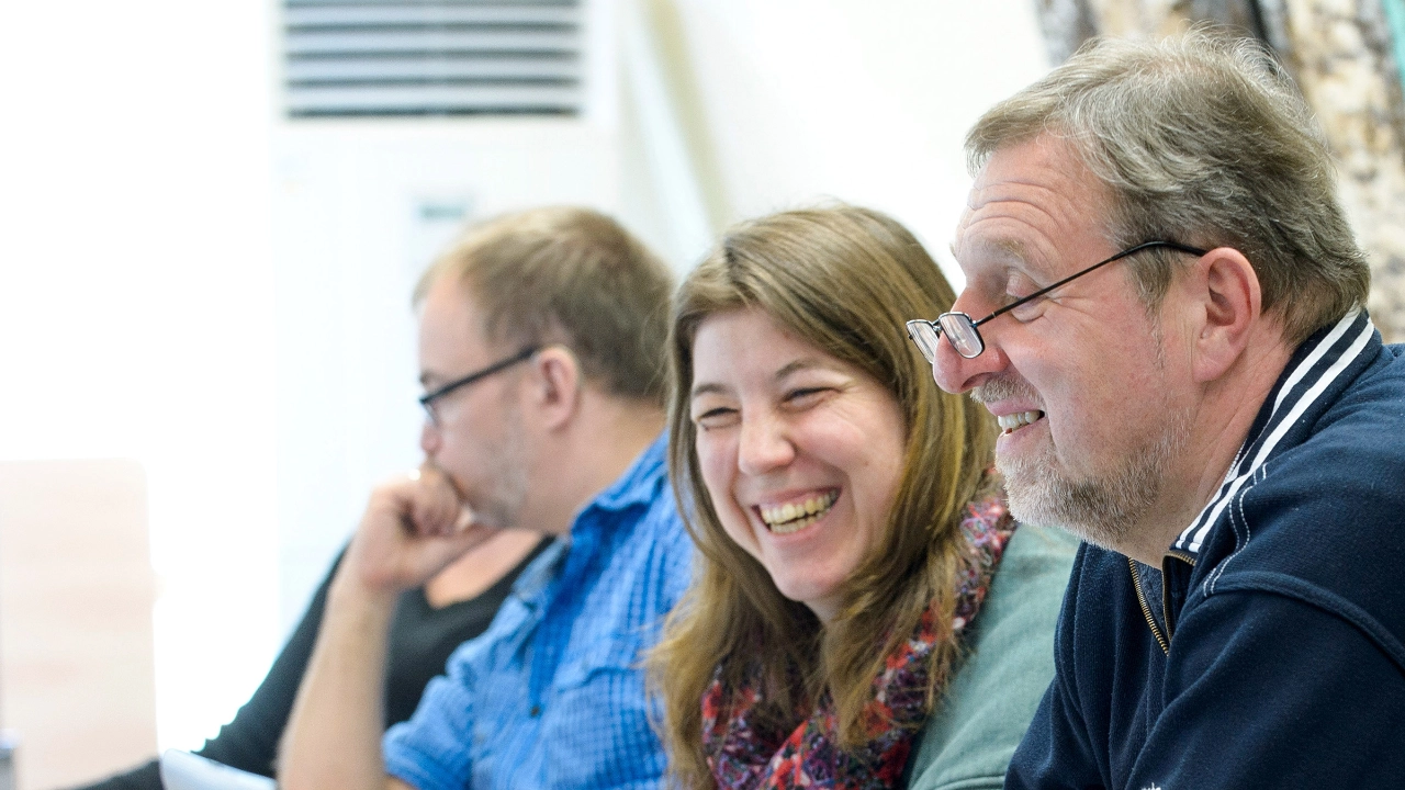 Drei ältere Männer und eine Frau lachend während eines Seminars.