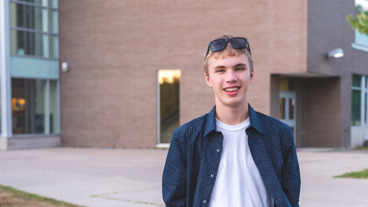 Junger Mann mit Sonnebrille auf dem Kopf steht vor einem Gebäude auf der Straße.
